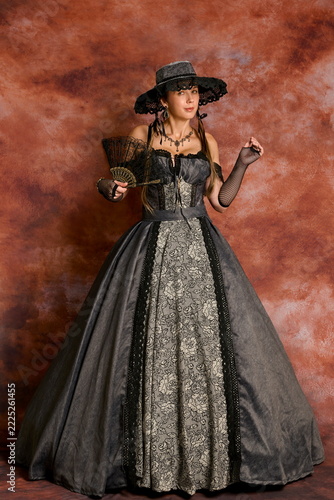 Elegant woman posing in in 19th-century Victorian gown and black hat