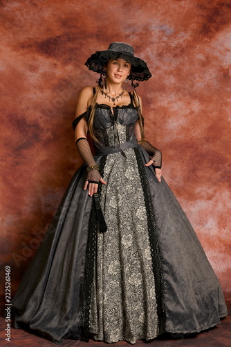 Elegant woman posing in in 19th-century Victorian gown and black hat
