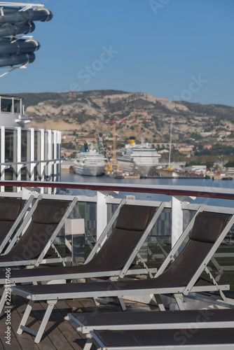 Pooldeck or swimmingpool with sun deck on modern cruiseship cruise ship liner in port with sun loungers ready for cruising to Mediterranean on sunny day with city skyline in background
