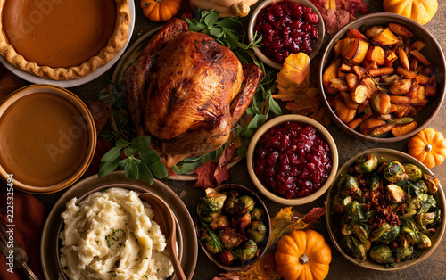 Roasted turkey garnished with sage leaves served alongside bowls of cranberry sauce mashed potatoes and seasonal vegetables.