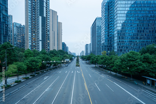 Empty urban road flanked by modern high-rise buildings and green trees