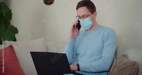 Masked man using smartphone and laptop at home