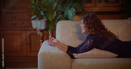 Smiling woman waving at smartphone while relaxing on a couch