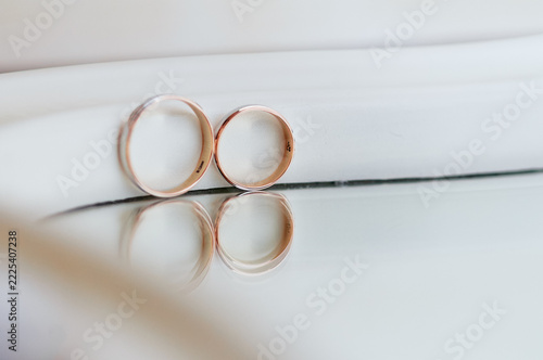 Obraz na plátně Two gold wedding rings rest against a pale background with a soft mirror reflection, evoking romance, commitment, intimacy and elegant minimalism for wedding, engagement and anniversary projects