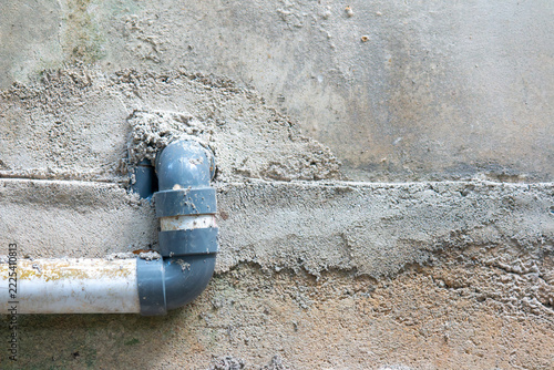 Gray PVC drain pipe with elbow fitting attached to a rough cement plastered wall with copy space on the right