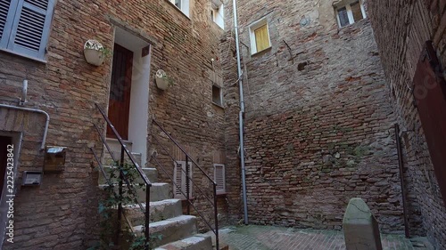 image shows a narrow courtyard with old brick buildings in Urbino, Italy