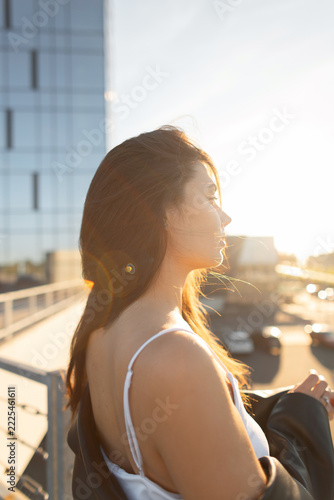 Fotografie A serene back-lit profile portrait of a young brunette woman in an urban setting at golden hour