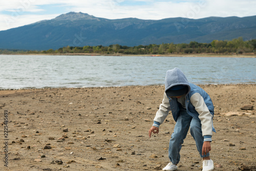 Child in hoodie picking stones at reservoir with low water level