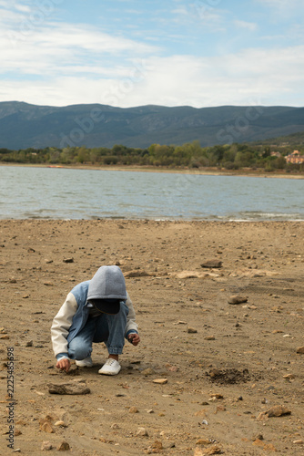 Child crouching on dry reservoir shore during drought, mountains