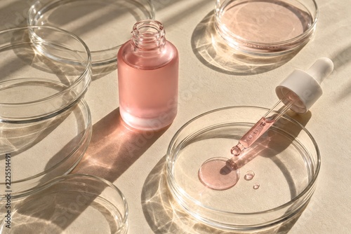 Pink serum bottle and glass pipette beside sunlit clear petri dishes