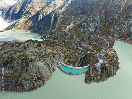 Top down aerial view of Grimselsee reservoir dam, historic hotel Grimsel Hospiz, and Aare river headwaters, Switzerland