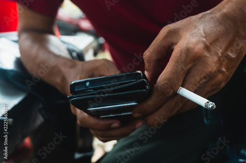 Close up of a man holding smartphone while holding a cigarette