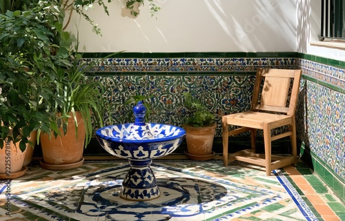 Andalusian courtyard with ceramic fountain, tiled floor, plants and wooden chair
