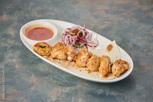Plate of grilled chicken pieces served with red dipping sauce sliced