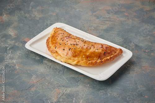 Golden-brown baked empanada on a white rectangular plate with sesame