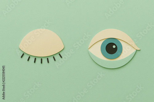 Eye, sleepy eye, closed eye, alert eye, eye fatigue, awareness concept, paper art of one sleepy dashed eyelid and one open alert eye with blue iris on soft green background