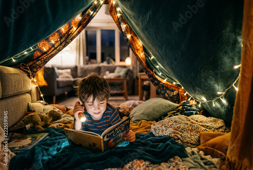 Child reading with a flashlight inside a living room blanket fort, view from inside the tent