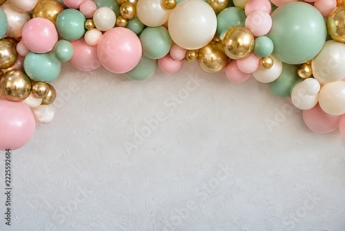 Pastel balloon garland with metallic gold accents above white textured wall