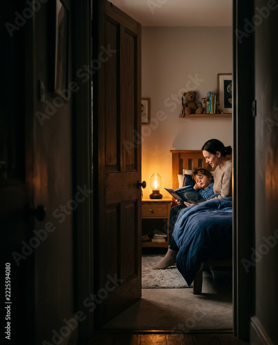 Parent reading a bedtime story to a sleepy child, seen through a slightly open bedroom door