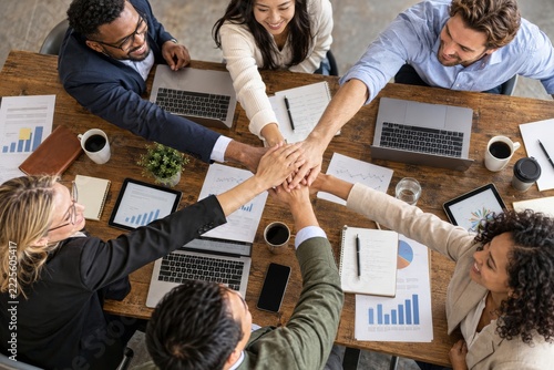 Overhead business team joins hands above laptops and reports on a wooden table