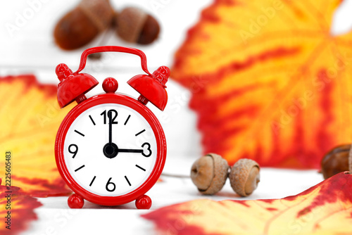 Red alarm clock with autumn leaves and acorns on a white background