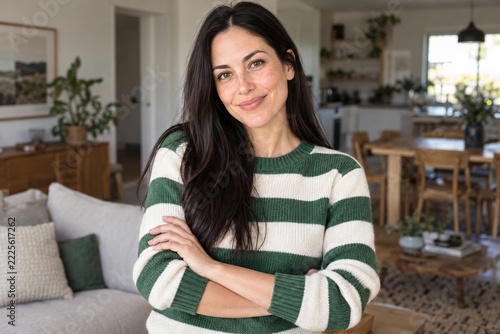 Smiling dark haired woman in a striped green sweater at home with folded arms