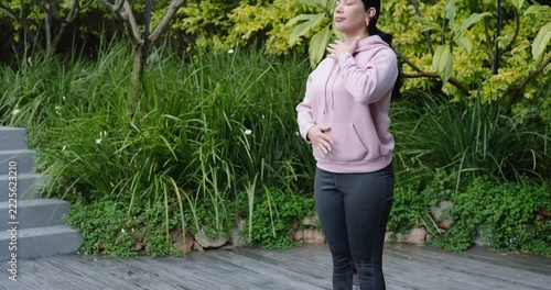 Woman folding, rising, placing hands on chest and belly, breathing, centering on yoga mat on deck