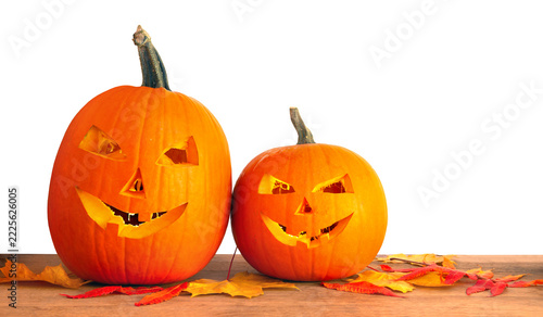 Two happy carved Halloween pumpkins with autumn maple leaves on wooden table over white background with copy space