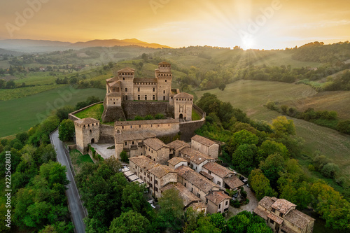 Aerial view of Torrechiara Castle and village on a hilltop at golden hour with sun flare over the Parma countryside