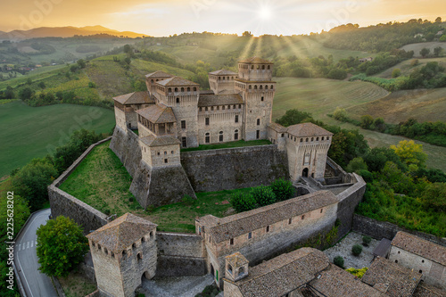 Aerial view of Torrechiara Castle and village on a hilltop at golden hour with sun flare over the Parma countryside