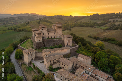 Aerial view of Torrechiara Castle and village on a hilltop at golden hour with sun flare over the Parma countryside