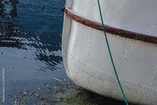 Weathered White Boat Hull with Rivets, Wooden Trim and Mooring Rope on Reflective Water