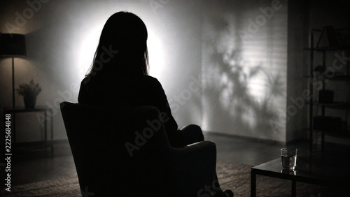 Silhouette of a woman sitting alone in a dark room with dramatic backlighting, expressing loneliness, isolation and emotional distress