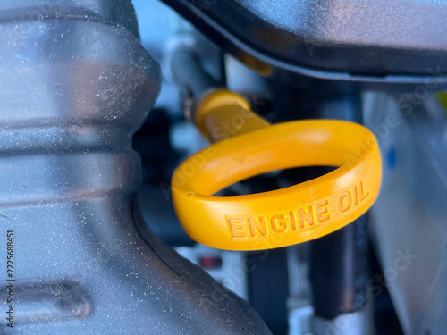 Close-up of a yellow engine oil dipstick handle inside an automobile engine compartment