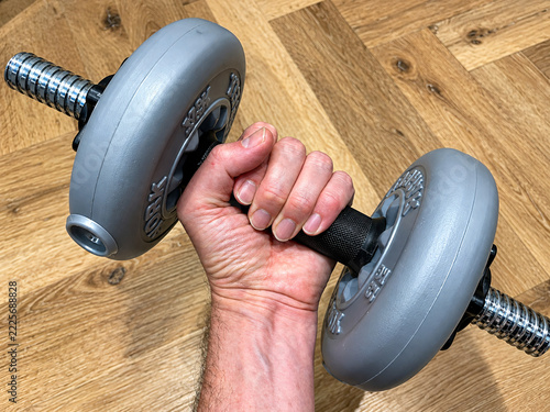 Close-up of a hand gripping a gray adjustable dumbbell over a wooden floor for strength training