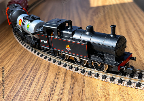 Detailed miniature steam locomotive curves across a model railway track in warm sunlight