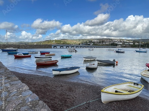 Small boats moored in a calm harbor beneath dramatic clouds and a coastal hillside village