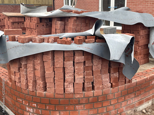 Stacks of red clay bricks covered with protective sheeting at a construction site