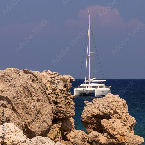 White Sailing Catamaran Near Rocky Coast of Rhodes, Greece