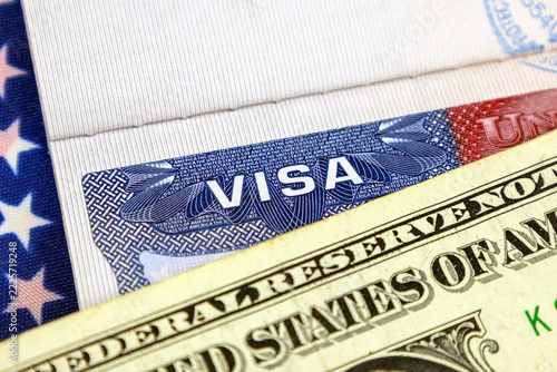 Macro view of USA visa document partly tucked beside US dollar bill on textured textile flag surface, highlighting travel paperwork, currency exchange, international trip planning, immigration