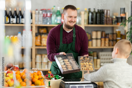 Friendly salesman kindly assisting little boy purchasing cookies in grocery store
