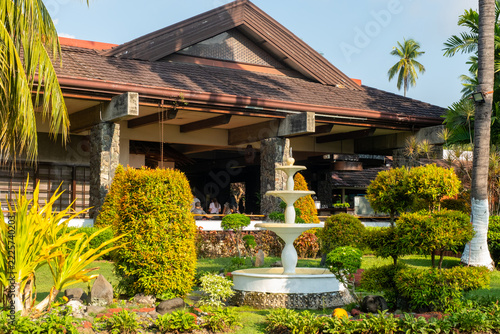 A large decorative sign stands among palm trees and garden plants at a tropical resort in Davao, Philippines, during daylight.