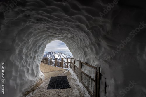 Entrance to a snow cave at the summit of Aiguille du Midi in the French Alps, providing access for alpinists exploring the high altitude mountain environment. Surrounded by thick snow, ice formations