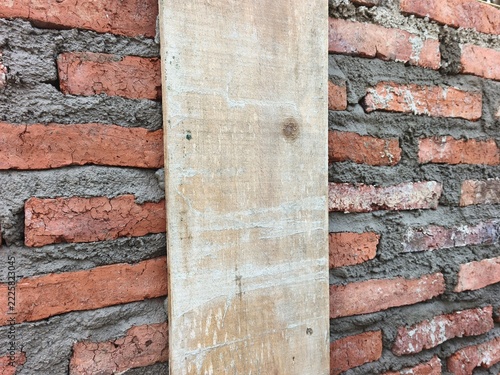 Close up of an unfinished red brick wall with wet cement mortar and a vertical wooden plank as a formwork column at a house construction site, perfect for architecture build photo