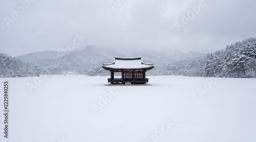 Snowy Pavilion on a Frozen Lake Surrounded by Majestic Mountains in a Winter Landscape