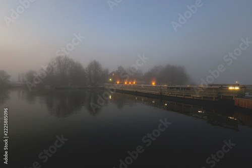 A wooden bridge leads to a small island in the early morning mist.