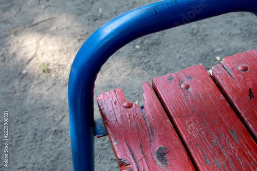 Weathered Red Wooden Bench with Blue Metal Frame in Playground