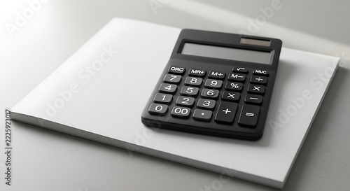 Black electronic calculator sitting on a white notebook grey desk