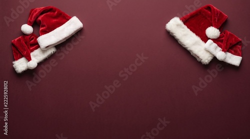 Two santa hats rest on a deep burgundy velvet background
