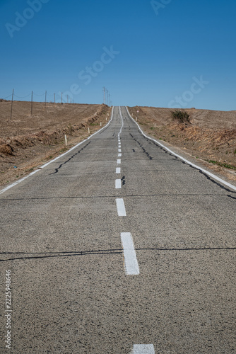 An old and worn asphalt road in a rural area. agricultural lands and blue sky background.
